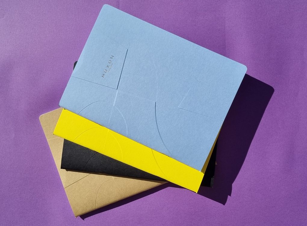 MOXON B5 ‘Form’ 52 Page Notebook in multiple colours stacked on a purple background with natural sunlight