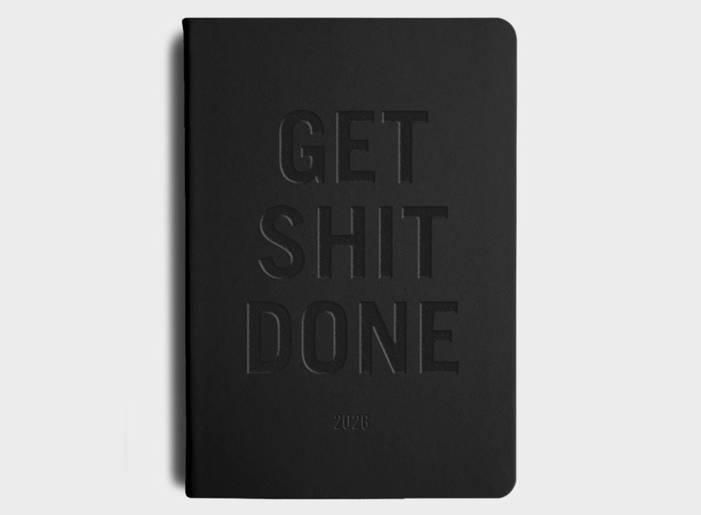 MiGoals GSD Weekly Spread goal setting diary  - Black Cover with Bold text saying "Get Shit Done" and the number "2026" embossed in the cover on a light beige background surrounded by other notebooks.
