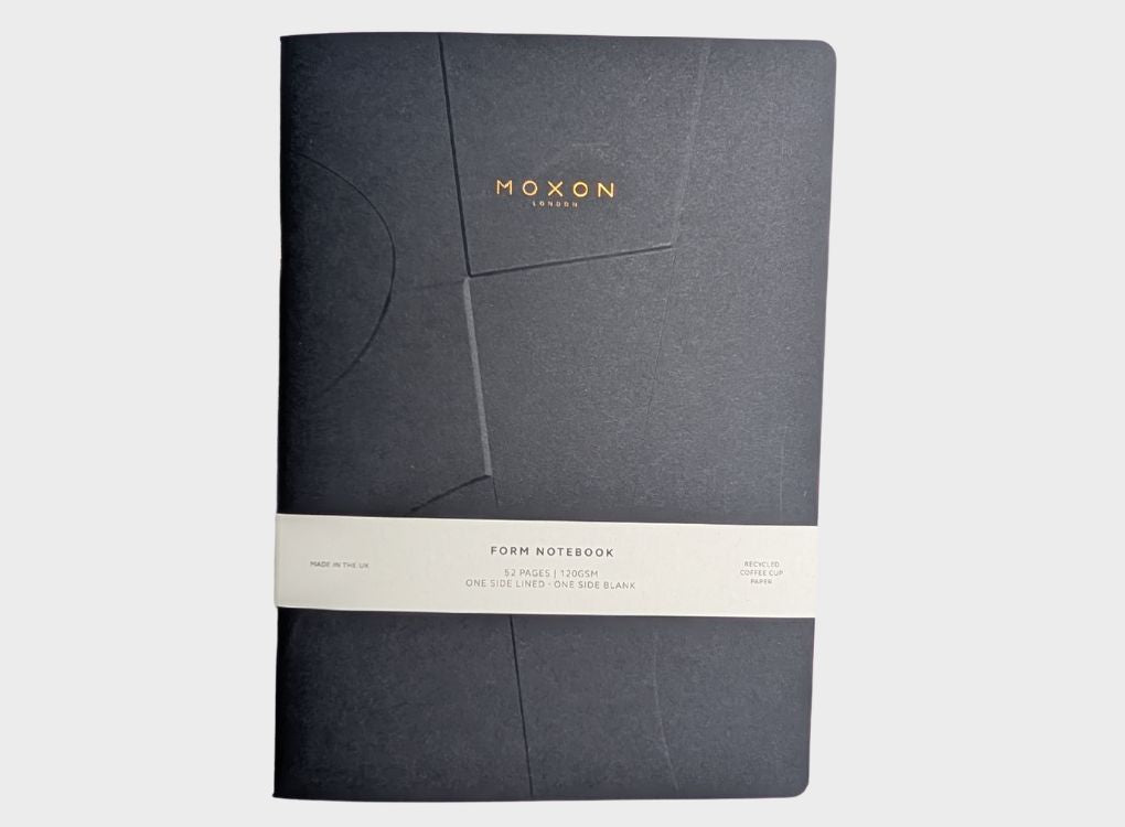 Black MOXON B5 ‘Form’ notebook with paper band packaging on a neutral background