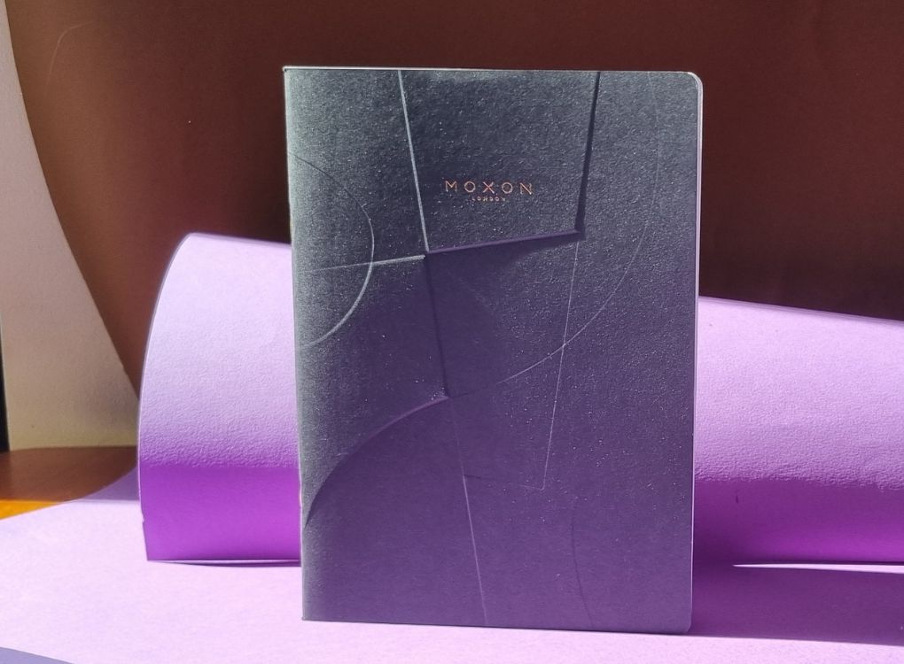 Black MOXON B5 ‘Form’ notebook standing upright with soft purple backdrop and lighting