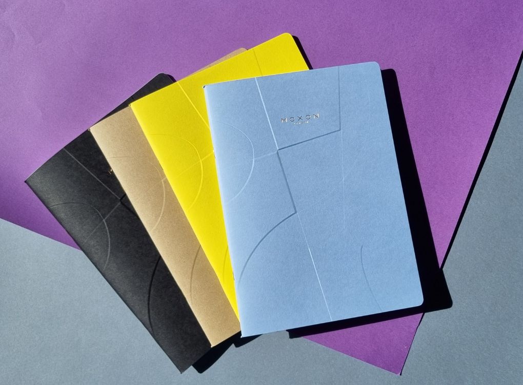 Blue, yellow, and black MOXON B5 ‘Form’ notebooks layered with bold lighting and shadows