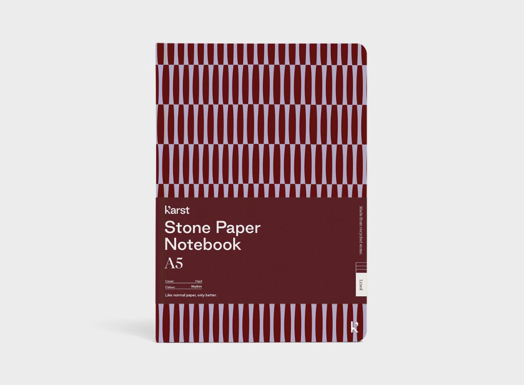 A Studio Muse A5 hardcover notebook by Karst with a maroon and lavender geometric patterned cover, displayed against a plain white background. The notebook features smooth, recycled stone paper with lined pages and a slim, lightweight cover.