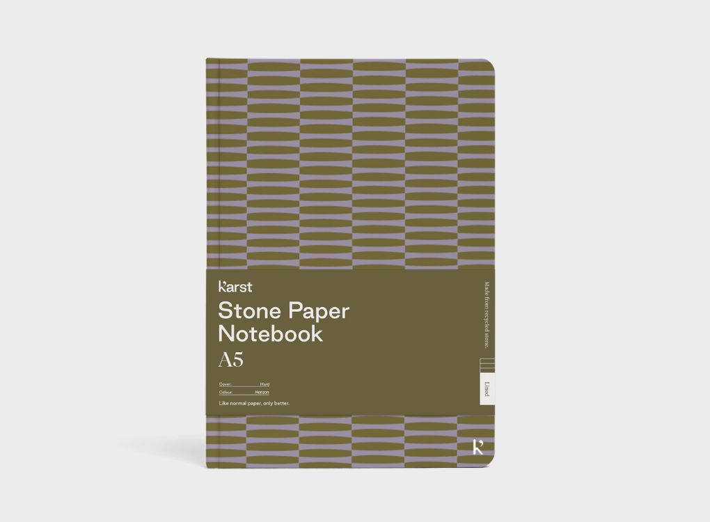 A Studio Muse A5 hardcover notebook by Karst with an olive green and lavender geometric patterned cover, shown against a plain white background. The notebook features smooth, recycled stone paper with lined pages and a slim, lightweight cover.