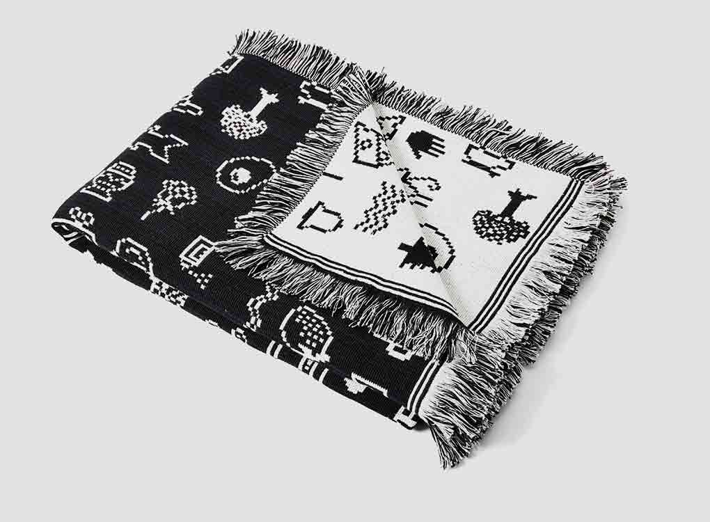 areaware cairo throw in black and white, laid flat, a large jacquard blanket-style throw with a contemporary print from old typefaces. A contemporary and interesting home accessory